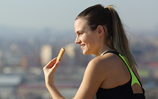 woman eating energy bar sitting outdoors after exercise in city outskirts