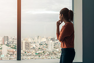 Young depressed asian woman standing alone near window in dark at evening time with low light environment, PTSD Mental health concept, Selective focus