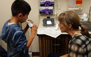 Catherine Karr, Ph.D., coaches a patient through an asthma test at the clinic
