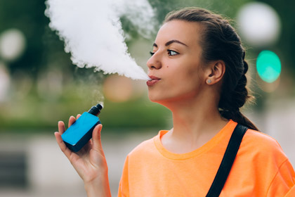 Picture of young woman vaping and blowing out smoke 