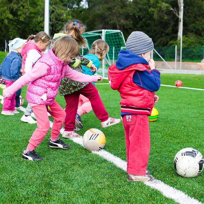 Children kicking soccer balls on astroturf field