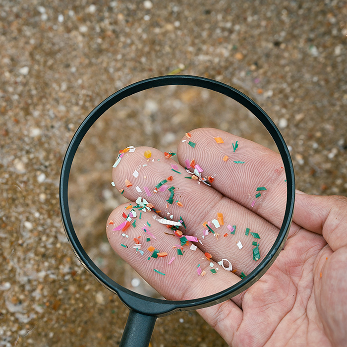 Magnifying glass be using to view microplastics in one's hand