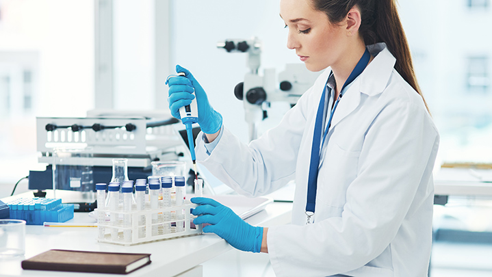 Scientist in protective gloves adding liquid to test tubes