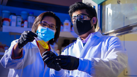 Two scientists in lab coats and face masks holding a sample