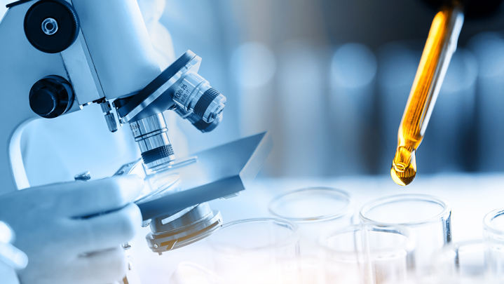 Microscope with laboratory glassware, dropping chemical liquid into test tube in lab.