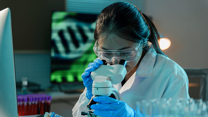 Scientist in protective gear looks into a microscope