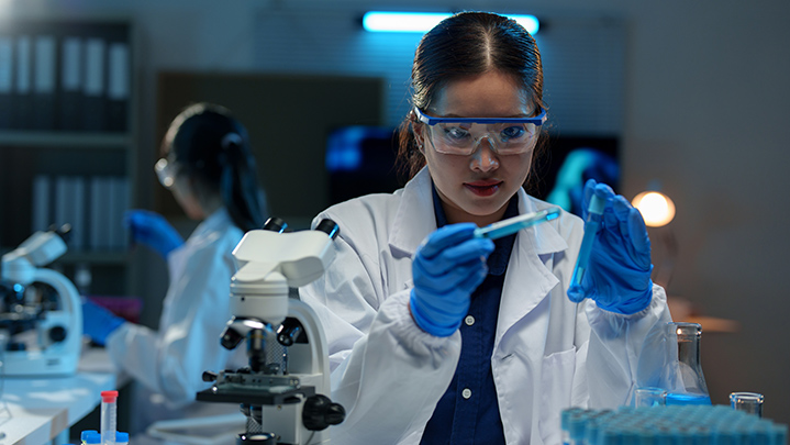 Asian female scientist holds a test tube filled with blue liquid in the laboratory.