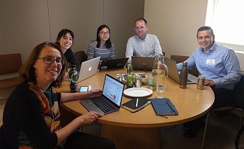 five men and women sitting around a circular table looking at computers