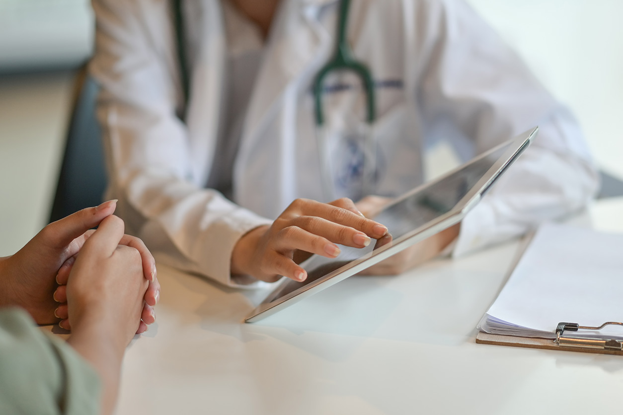 Patient and doctor look over iPad and clipboard while sitting at table