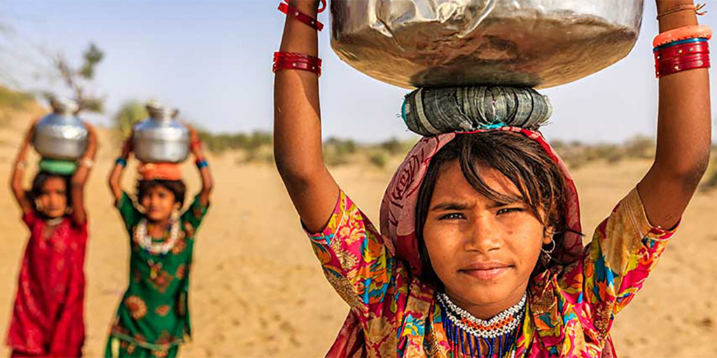 girls crossing sand dunes and carrying water on their heads
