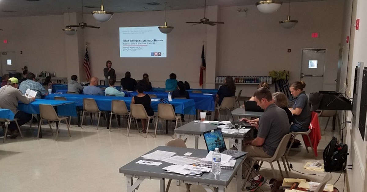 room of people sitting around tables with information showing on a projection screen