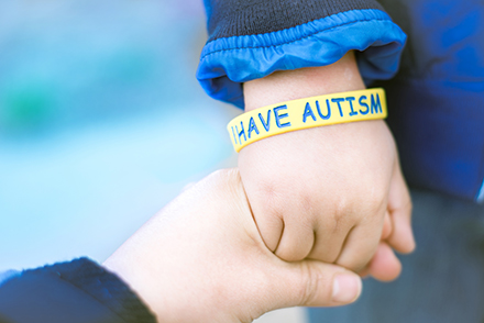 child's hand with wristband reading "I have Autism"