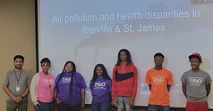 Group of students standing together at the front of a lecture hall with their presentation displayed behind them