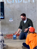 Man standing in front of a group of children showing them a sampling device