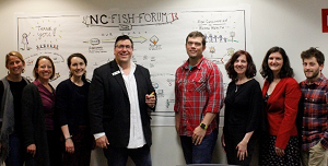 Group photo in front of a visual poster of notes from the Fish Forum