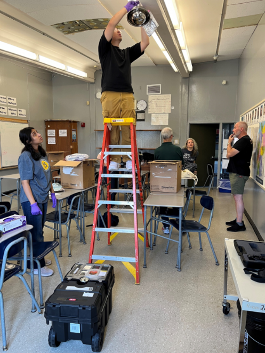 Man on step ladder attaching device to classroom ceiling