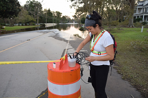 Woman collecting floodwater samples on a street next to a traffic cone