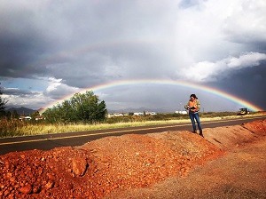Person standing on a road with a rainbow overhead