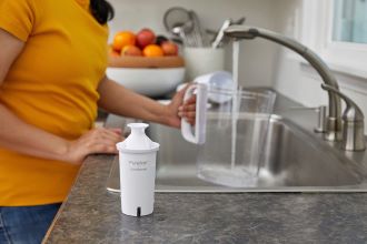 Cyclopure filter, in background a woman fills a filtered water pitcher.