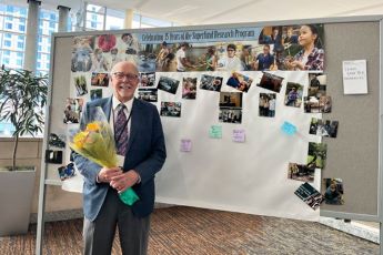 Bill Suk standing in front of memory wall, in his honor, at the 2022 SRP Annual Meeting.