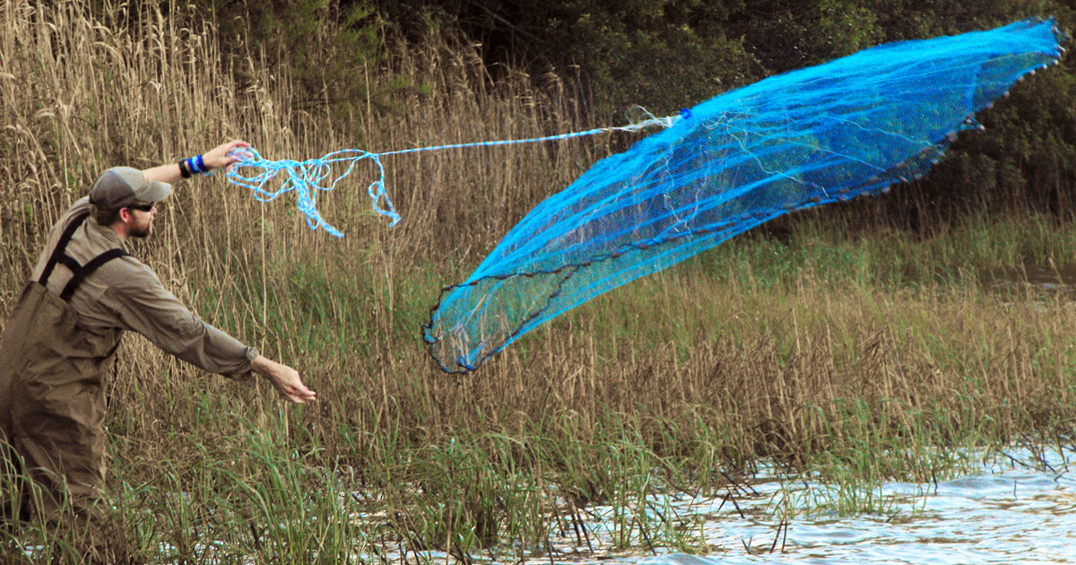 person throwing a fishing net into a lake