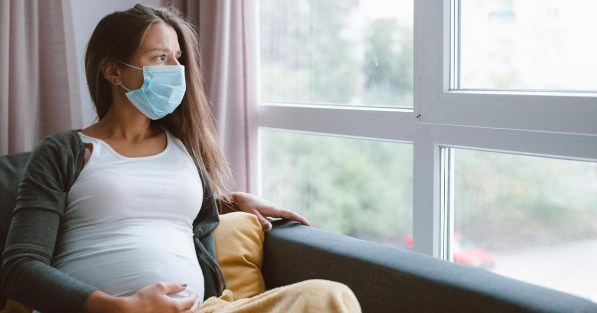 pregnant woman wearing a mask looking out a window