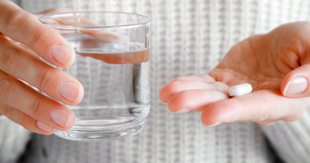person holding a pill and a glass of water