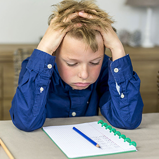boy staring at notebook while holding his head