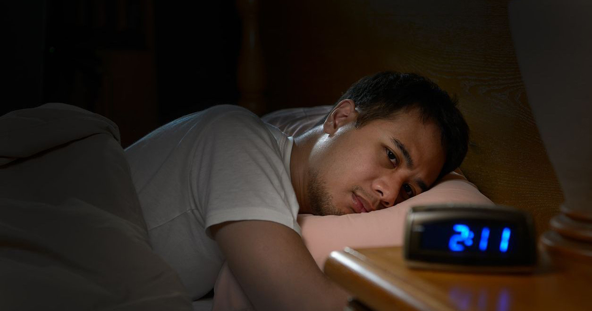 man lying down in bed late at night while looking at clock on side table