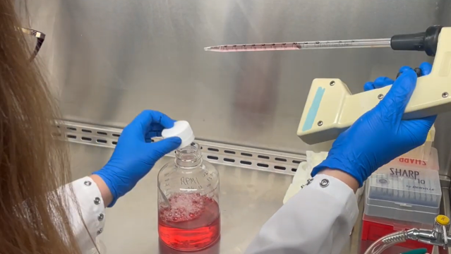 Woman in lab holding pipette over a bottle of red liquid