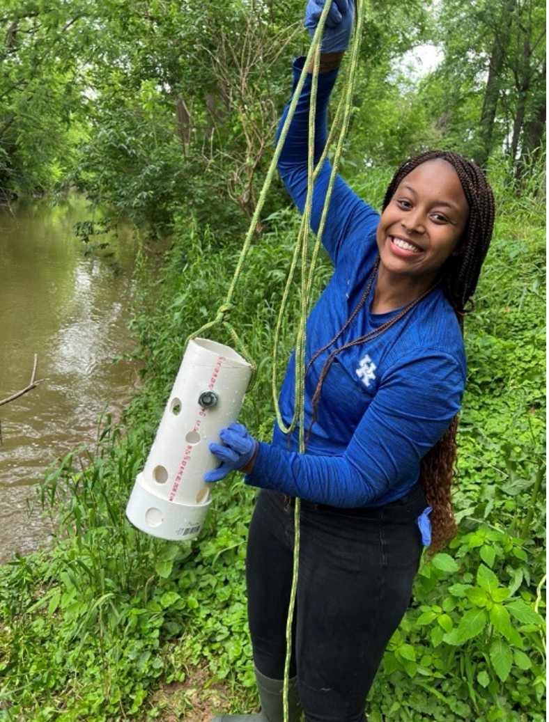 Ariel holding up field equipment on the bank of a river