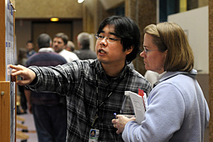 Asian teen boy talking to woman scientist in front of science project