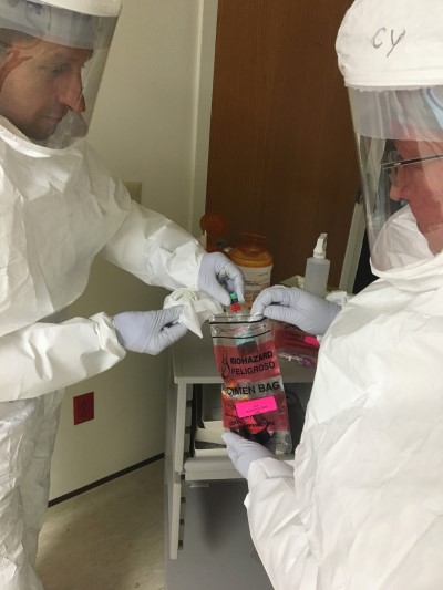 Two workers in HAZMAT suits putting a biohazard in a specimen bag