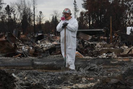 Worker in HAZMAT suit standing in charred debris after a wildfire