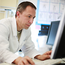 man wearing a white lab coat sitting in front of a computer
