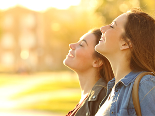 2 women in profile with eyes closed and smiling outside on a sunny day