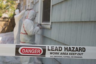 workers removing lead from house paint with lead hazard sign