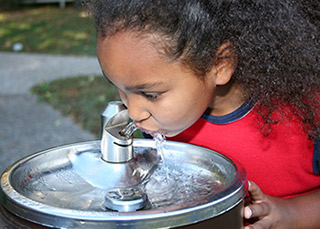 Niña bebiendo de una fuente de agua