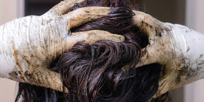 Woman wearing rubber gloves applying hair dye to her hair