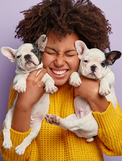 woman smiling wide while holding two dogs close to her face
