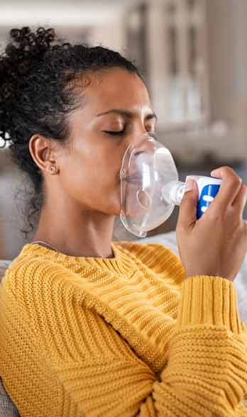 woman sitting on couch using a breathing device
