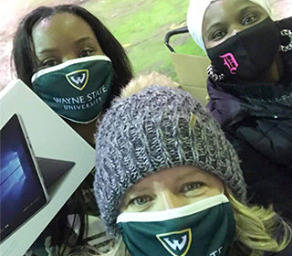 three volunteers in warm clothes and facemasks holding a new computer