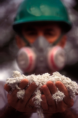 Worker holding handfuls of asbestos product while wearing respirator