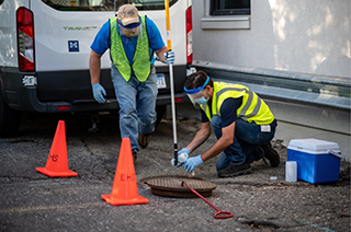 men collecting sewage samples beside a manhole