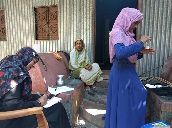 Photograph of two women sitting, and one woman standing walking away from them