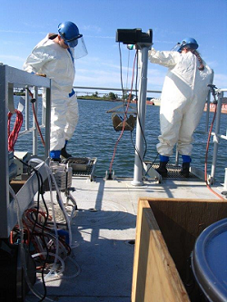 Two people in hazmat suits standing on the deck of a boat with sampling equipment