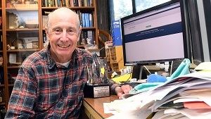 man sitting in an office with a computer and large stack of papers