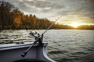 fishing rod on side of boat with a coastline of trees and a sunrise