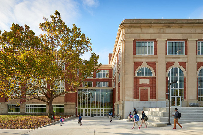 Exterior view of a school building with people walking outside carrying backpacks