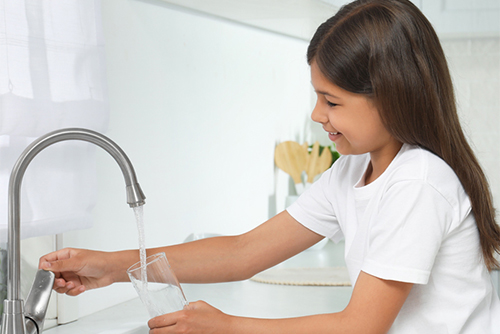 child filling a glass of water from the sink